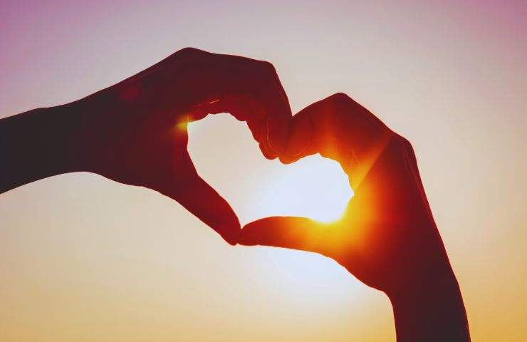 mani formano cuore davanti al sole