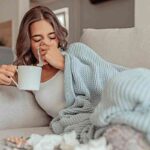 Donna influenzata sul divano di casa con tazza in mano
