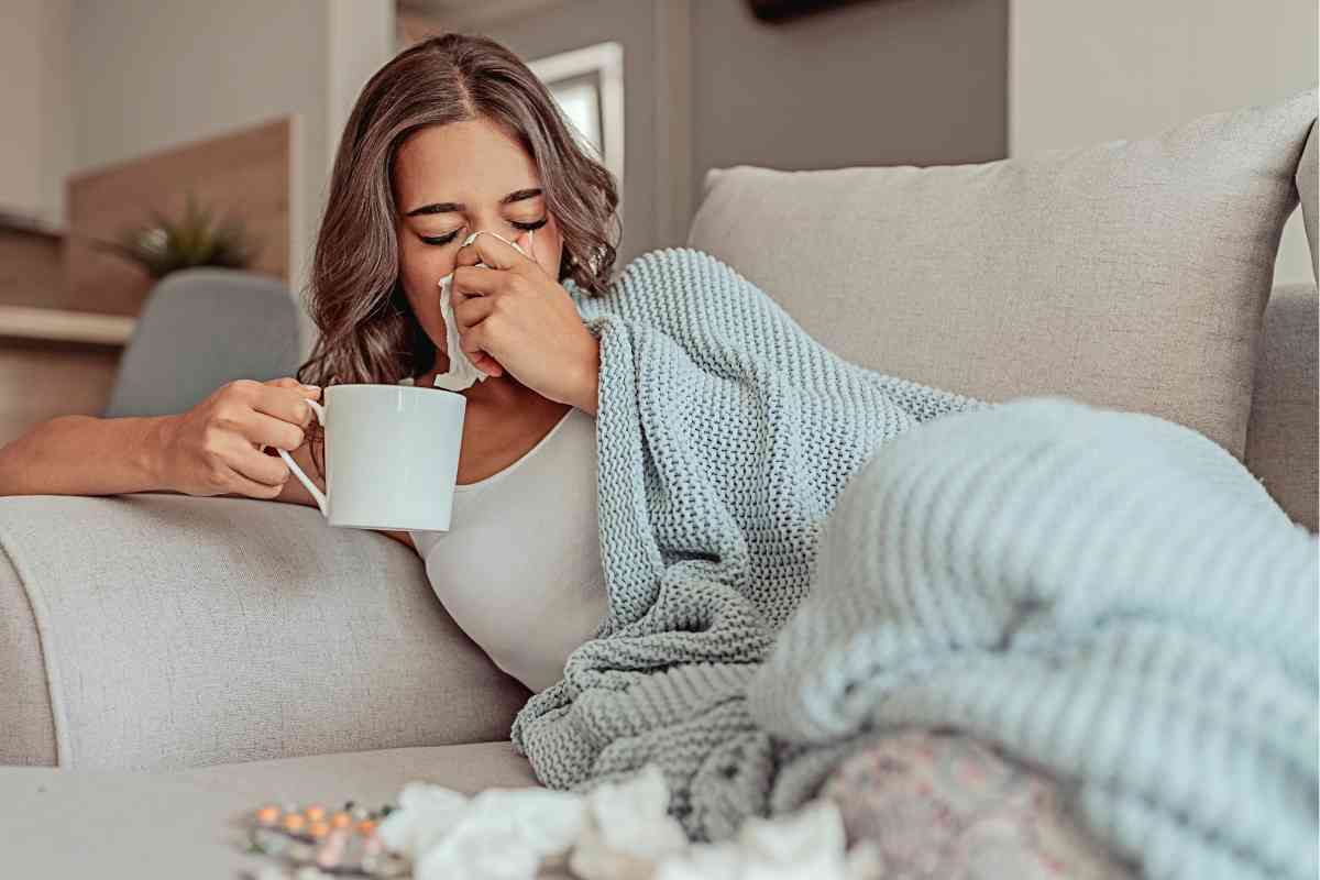 Donna influenzata sul divano di casa con tazza in mano