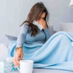 Una donna ammalata si soffia il naso e prende una tazza