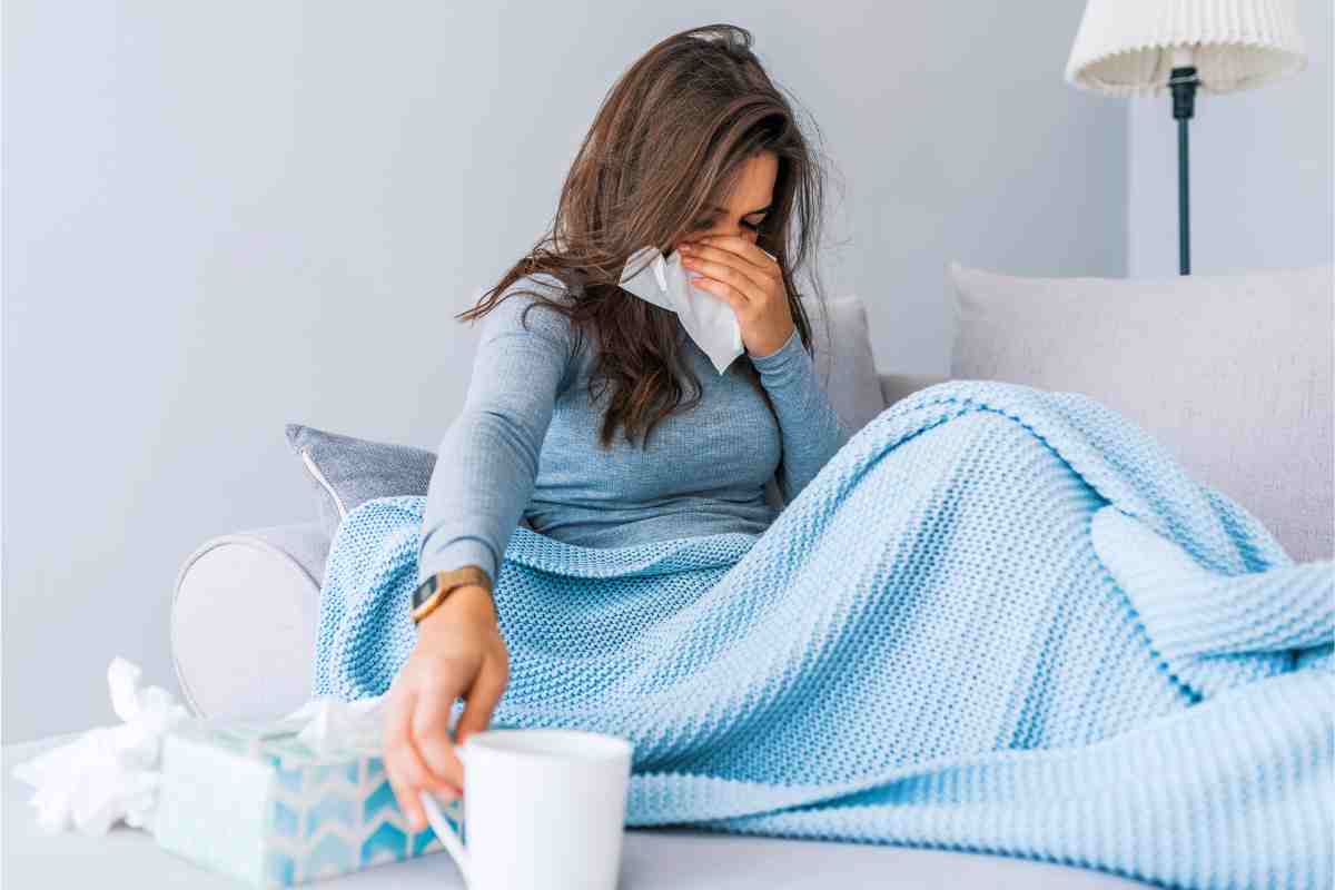 Una donna ammalata si soffia il naso e prende una tazza