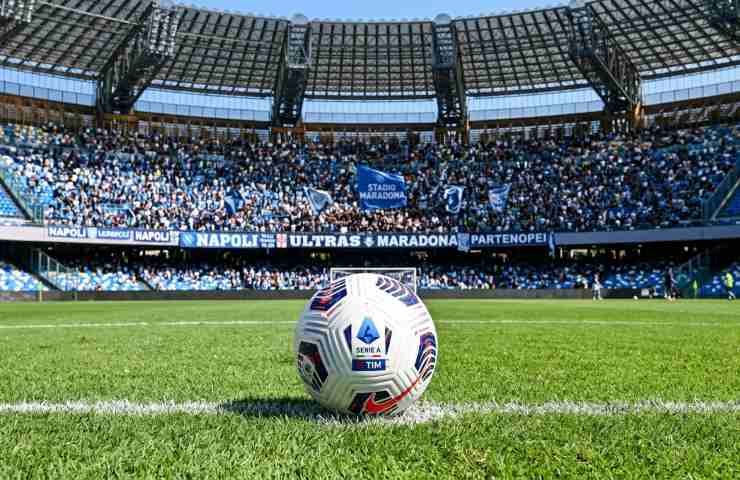 Pallone ufficiale della Serie A sul prato verde dello Stadio Diego Armando Maradona di Napoli durante una partita: lo stadio è gremito di tifosi e i loghi "STADIO MARADONA", "ULTRAS" e "NAPOLI" sono visibili sulle tribune.