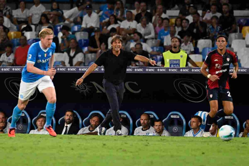 Antonio Conte sullo sfondo con Kevin De Bruyne del Napoli e Gabriele Zappa del Cagliari in campo.