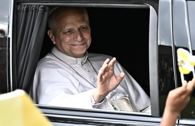 Papa Leone XIV saluta con il braccio destro alzato dal finestrino di un'auto.