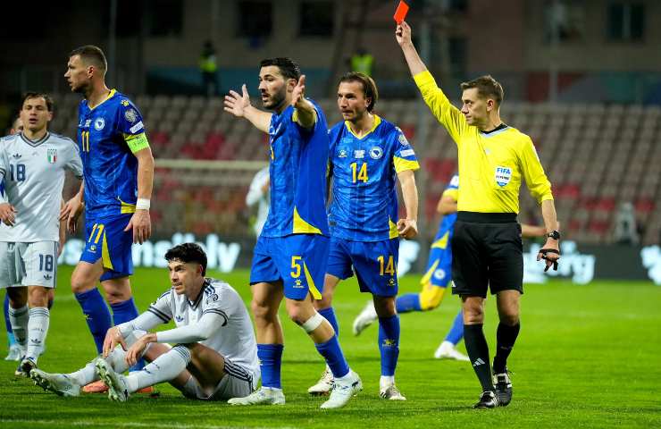 L'arbitro francese Clement Turpin mostra il cartellino rosso ad Alessandro Bastoni seduto a terra in Bosnia-Italia circondato da avversari bosniaci.