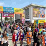 Ingresso del COMICON Napoli 2026 alla Mostra d’Oltremare con folla di visitatori, cosplayer di Goku e Spider-Man, e cartelloni ufficiali di Leo Ortolani e Kazuhiko Torishima durante una giornata di sole.