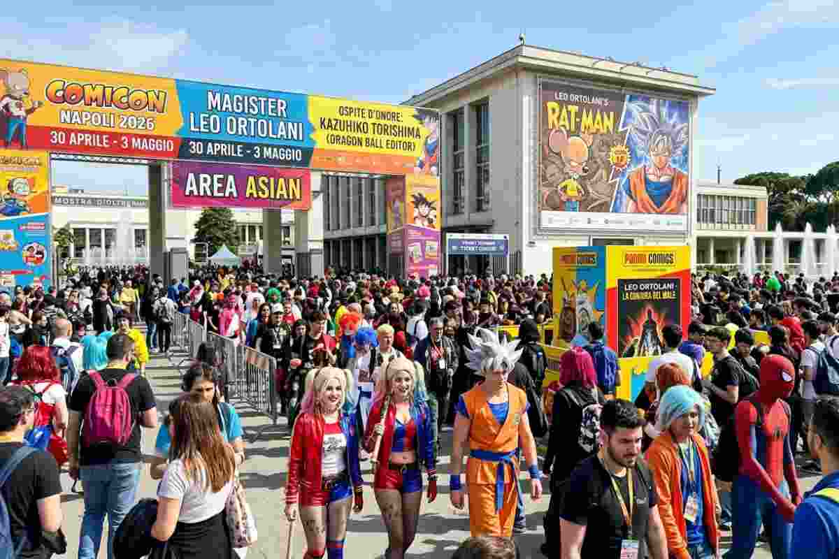 Ingresso del COMICON Napoli 2026 alla Mostra d’Oltremare con folla di visitatori, cosplayer di Goku e Spider-Man, e cartelloni ufficiali di Leo Ortolani e Kazuhiko Torishima durante una giornata di sole.