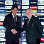 Antonio Conte ed Aurelio De Laurentiis si stringono la mano al cospetto dell'obiettivo con un pannello degli sponsor come sfondo.