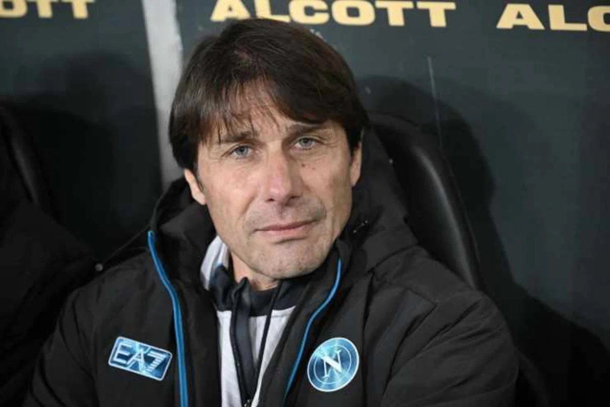 Antonio Conte con la tuta di rapprsentanza del Napoli seduto in panchina mentre guarda verso l'obiettivo.