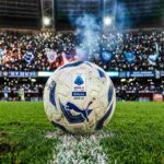 Pallone Serie A 2025-26 a centrocampo dello Stadio Maradona di notte per Napoli-Milan, tifosi e luci sugli spalti.