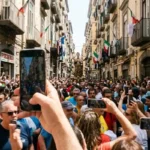 Folla in via dei Tribunali a Napoli durante la processione di San Gennaro con turisti e smartphone.