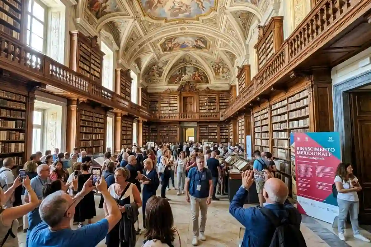 Inaugurazione mostra Rinascimento Meridionale alla Biblioteca dei Girolamini a Napoli: visitatori scattano foto nella sala monumentale barocca piena di libri.