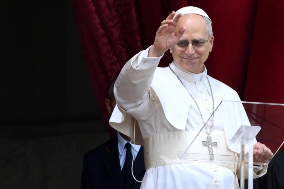 Papa Leone XIV sorride mentre saluta la folla davanti a sé col braccio destro alzato.