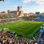Stadio Ennio Tardini di Parma gremito per la partita di Serie A Parma-Napoli: tifosi del Parma in gialloblù a sinistra e tifosi del Napoli in azzurro a destra si circondano la struttura e il campo da gioco.