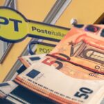 Sullo sfondo un ufficio di Poste Italiane, in primo piano un mazzetto di banconote da 50 euro